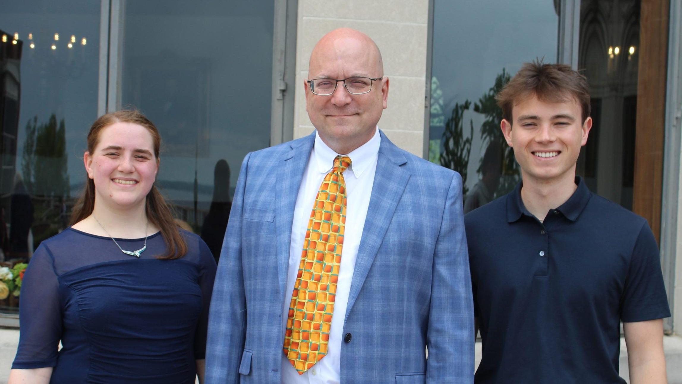 澳博体育app下载 scholarship recipients wearing navy blue shirts stand next to 澳博体育app下载's technical services manager wearing a yellow tie and blue plaid sportcoat.